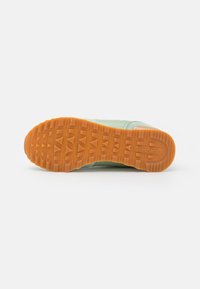 Baskets vertes avec une semelle en caoutchouc texturée orange, présentant une tige en tissu doux et une zone rembourrée autour du talon.