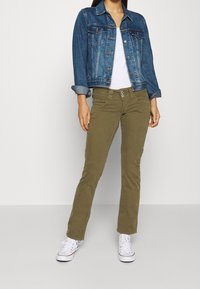 Džínová bunda s modrým omdlením, zapínání na knoflíky a dvě náprsní kapsy. Olivově zelené rovné kalhoty s dvěma předními kapsami a dvojitým knoflíkem. Bílé tenisky.