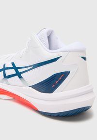 White athletic shoe with a textured upper, blue accents, and red detailing on the sole. Features a low profile and supportive heel design.