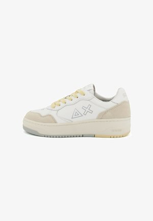 Baskets en cuir blanc avec des accents en daim beige, dotées d'une semelle épaisse, de lacets jaunes et d'un design de logo sur le côté.