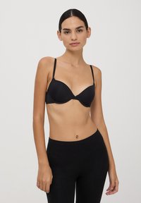 Reggiseno push-up nero con sottili spalline regolabili, coppe senza cuciture e una finitura opaca liscia, abbinato a leggins neri attillati.