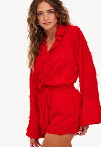 Ensemble rouge en deux pièces en tissu texturé, composé d'une chemise à col et à boutons à manches longues et d'un short assorti avec une taille à cordon.