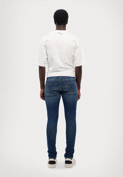 T-shirt bianco a maniche corte e jeans blu slim fit con cuciture arancioni. I jeans presentano due tasche posteriori e una silhouette snella.