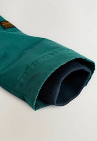 Manche de veste verte avec un tissu extérieur lisse et une doublure intérieure en velours bleu marine. Comprend un ourlet cousu et aucun matériel visible.