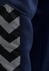 Gros plan d'un tissu bleu marine avec un détail de motif chevron noir et blanc cousu sur un matériau textile texturé.