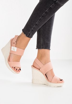 Sandales compensées roses avec deux larges brides en tissu, talon texturé de style espadrille. Caractérisées par un bout ouvert et un vernis à ongles noir.