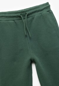 Zielone joggery o splocie wafelowym z elastycznym pasem i sznurkiem. Teksturowany materiał w luźnym kroju. Brak widocznych kieszeni.