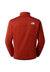 Fleece jas in roestrode kleur met een opstaande kraag, lange mouwen en een zwarte zoom. Heeft een wit logo op de bovenrug.