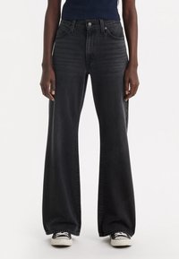 Czarne dzwony z wysokim stanem wykonane z denimu o luźnym kroju. Posiadają przednie kieszenie, klasyczne zapięcie na guzik oraz delikatne przecierania na nogawkach.