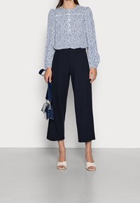 Bílá blůza s modrými puntíky, nařasené ramena; námořnické culottes; béžové sandály na podpatku s otevřenou špičkou; malá modrá kabelka.