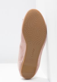 Semelle d'une chaussure plate en daim rose avec une semelle extérieure en caoutchouc texturée présentant des motifs ondulés et la marque "Gabor", fabriquée en Slovaquie.