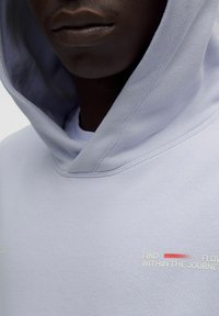Lys grå hoodie med en blød struktur, der har et front-slogan: "FIND FLOW INDTIL REJSEN," og en dyb hætte for dækning.