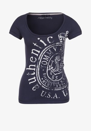 Námořnická modrá tílko s krátkým rukávem a kulatým výstřihem, které má bílé potištěné grafiky, včetně kotvy a textu "autentické".