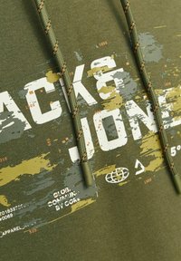 Olijf groene hoodie van zachte stof met een wit en geel gestructureerd patroon. Bevat dikke trekkoorden met ribbeluiteinden en grafische details.