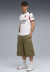 Valkoinen urheilupaita mustilla ja punaisilla korostuksilla, yhdistetty oliivinvihreisiin cargo-shortseihin. Valkoiset lenkkarit ja sukat täydentävät asun.