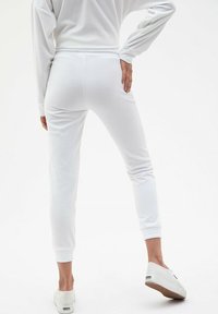 Białe dresowe spodnie o zwężającym się kroju, z elastycznym pasem i ściągaczami na nogawkach. Gładka faktura materiału bez widocznych wzorów czy akcentów.