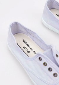 Scarpe di tela viola chiaro con profilo basso, suola in gomma bianca e cinque occhielli metallici per i lacci. Interno etichettato con il nome del marchio e dettagli per la cura.