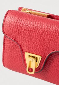 Červená texturovaná kožená peněženka se zlatou obdélníkovou sponou, na které je na přední klopě vyryto "COCCINELLE".