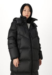 Black puffy coat with a zip front, high collar, and detachable hood. Features oversized quilted panels and elastic cuffs for a snug fit.