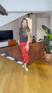 Κόκκινη φλοράλ φούστα με καμπυλωτό τελείωμα, συνδυασμένη με ένα στενό γκρι τοπ. Η φούστα έχει έντυπη ζωντανών χρωμάτων και η τοποθεσία είναι ένα σύγχρονο σαλόνι.