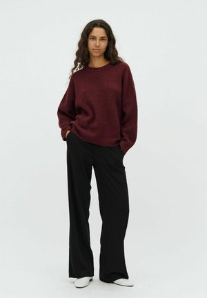 Burgundy ribbed sweater with long sleeves, paired with black wide-leg trousers and white slip-on shoes. Plain background for contrast.