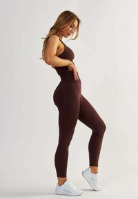 Hnědý žebrovaný sportovní set obsahující crop top a legíny s vysokým pasem, doplněný o bílé tenisky. Hladká textura, přiléhavý design.