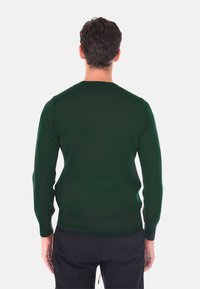 Maglione verde scuro, slim fit, scollatura rotonda, maniche lunghe, texture a coste e orlo. Indossato con pantaloni neri; la vista posteriore mostra un design senza cuciture.