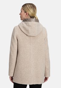 Beige, getextureerde jas met een capuchon, voorzien van een gladde, lichtgekleurde voering. Rechte snit met lange mouwen en geen zichtbare sluitingen.