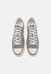 Sneakers in tela grigia con punta in gomma nera, lacci bianchi e logo "Converse All Star" sulla linguetta. Presentano dettagli di cucitura bianchi.