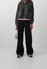 Grå denimjacka med huva och elastiskt avslut, ihop med svarta vida byxor och silverfärgad crossbody-väska. Sneakers fulländar outfiten.