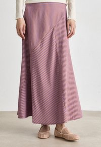 Jupe maxi rayée violet et orange avec un parement diagonal. Tissu doux, design fluide, associée à des ballerines en maille à lacets.