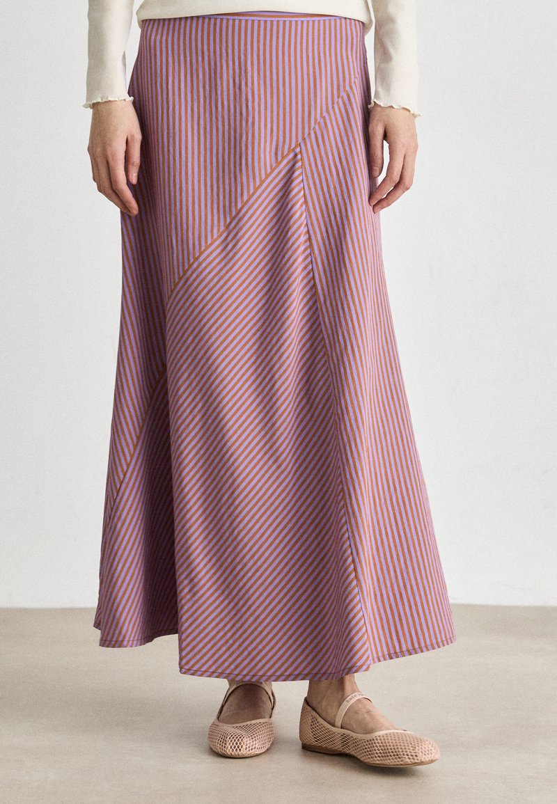 Jupe maxi rayée violet et orange avec un parement diagonal. Tissu doux, design fluide, associée à des ballerines en maille à lacets.