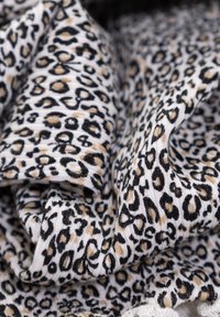 Tessuto in stampa leopardata, caratterizzato da macchie nere e marrone chiaro su uno sfondo bianco, con una texture morbida e un aspetto stropicciato.