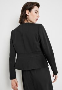 Schwarze maßgeschneiderte Jacke mit Peplum-Design, langen Ärmeln und glatter Textur; sie verfügt über strukturierte Nähte und einen minimalistischen Stil.