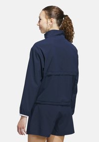 Navy blue, ribbed fabric jacket with a high collar and elastic cuffs, layered design at the back. Paired with matching shorts.