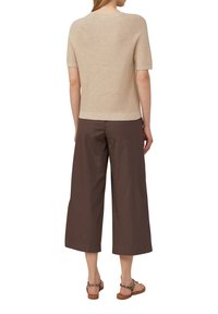 Hellbeige gestricktes Oberteil mit kurzen Ärmeln, kombiniert mit weit geschnittenen braunen Caprihosen und braunen Sandalen. Der Stoff wirkt weich und strukturiert.