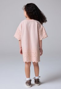 Vestido de algodón rosa con bordado de encaje en el dobladillo y las mangas, con bordes ondulados. Combinado con zapatillas de estampado de leopardo.