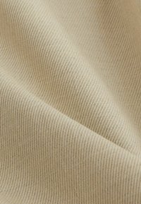 Gros plan d'un tissu beige avec une fine texture côtelée verticale et des plis doux créant des ombres délicates.
