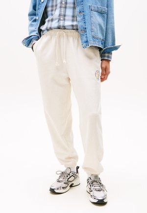 Pantalones de chándal color crema con cintura elástica y cordón. Cuenta con bolsillos laterales y un logo bordado colorido cerca del muslo.