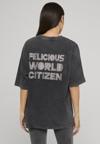 Přehnaně velká černá košile z měkké, ošoupané látky s kulatým výstřihem; na zádech nápis z kamínků: „FELICIOUS WORLD CITIZEN“.