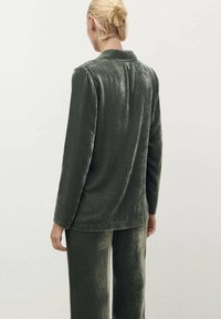 Conjunto de loungewear de terciopelo en un suave tono verde oliva. Presenta una parte superior de manga larga con un cuello sencillo y pantalones a juego, mostrando una textura suave.