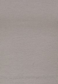 Camiseta sin mangas de tejido acanalado gris claro con una textura suave, un diseño ajustado y costuras a lo largo del dobladillo. Sin logotipos ni patrones visibles.