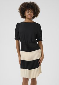 Svart och creamfärgad plisserad klänning med en figurnära bodice, puffärmar och ett kontrasterande horisontellt randmönster vid fållen. Mjuk tygtextur.
