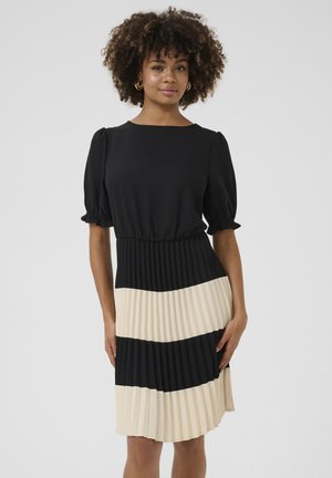 Svart och creamfärgad plisserad klänning med en figurnära bodice, puffärmar och ett kontrasterande horisontellt randmönster vid fållen. Mjuk tygtextur.
