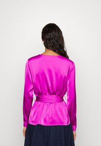Blusa in raso rosa con maniche lunghe, vita aderente con laccio, orlo a peplum e polsini con bottoni. Texture liscia, con un semplice scollo rotondo.