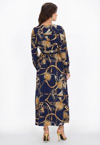 Marineblaues Kleid mit langen Ärmeln, Gold floralem und Kettenprint, tailliertem Schnitt und fließendem Rock, kombiniert mit schwarzen Absätzen.