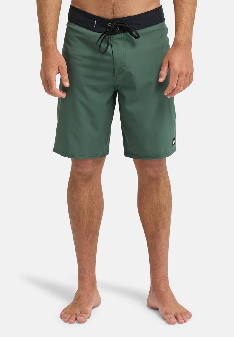 Groene zwembroek met een zwarte tailleband met trekkoord. Gemaakt van glad, lichtgewicht stof. Heeft een klein logo aan de onderkant aan de linkerkant.