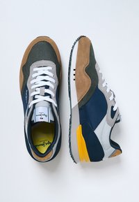Baskets avec un dessus en matériaux mélangés présentant des teintes marine, grise et brune ; lacets blancs ; accents jaunes au niveau du talon ; semelle noire texturée.