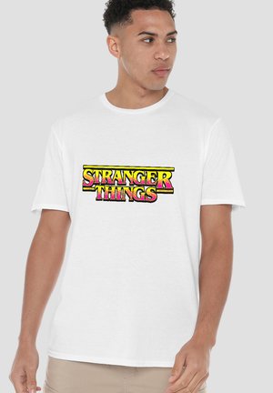 White cotton t-shirt featuring a colorful "STRANGER THINGS" logo in pink and yellow with a bold, retro design. Short sleeves and crew neck.