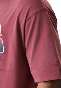 Bordeauxfarbendes T-Shirt aus weicher Baumwolle, mit rundem Halsausschnitt und einem kleinen Logodetail, das auf dem Ärmelsaum gestickt ist. Glatte Textur.